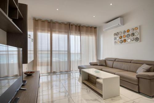 a living room with a couch and a tv at Malta's Beachfront Apartment in Mellieha in Mellieħa