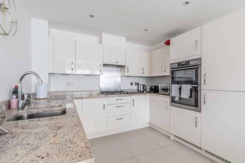 a white kitchen with white cabinets and appliances at STYLISH 4 BED 2 BATH & PARKING - PINEWOOD HEATHROW - By Tempstay in Slough