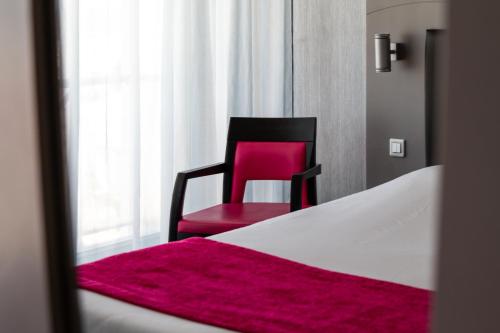 a red chair sitting next to a bed with a pink blanket at Hôtel Le Nautic in Arcachon
