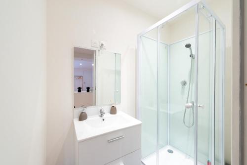 La salle de bains blanche est pourvue d'un lavabo et d'une douche. dans l'établissement COSY LOCATION - Confortable, cosy et équipé - Places gratuites à proximité, à Anzin