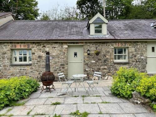a stone house with a grill and chairs in front of it at Crug Yr Eryr Isaf in Llandysul