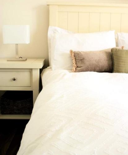 a white bed with a lamp on a night stand at Cozy & Remote Hideaway Gintys Cottage in Ross Port
