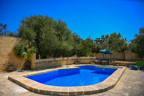 a swimming pool in a yard with a table and an umbrella at Villa Xini in Xewkija