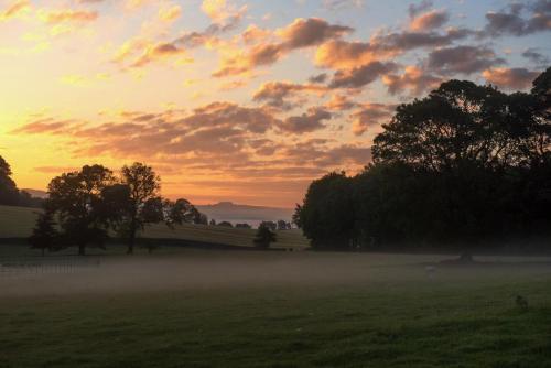 a sunset over a field with trees in a field at Low Lodge at Broughton Sanctuary in Skipton