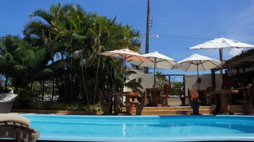 a swimming pool with umbrellas and tables and chairs at Hotel Aconchego Porto de Galinhas in Porto De Galinhas