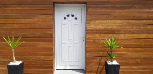 a white door on a wooden wall with two potted plants at Casa do Sossego - Guesthouse in Rabo de Peixe