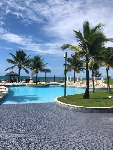 a swimming pool with palm trees and the ocean at Flat no Beach Class Muro Alto in Porto De Galinhas