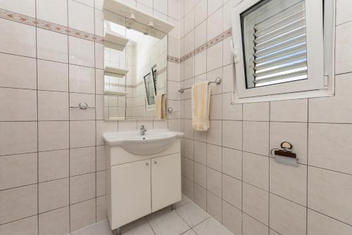 baño blanco con lavabo y ventana en Apartmani Petracie, en Drvenik