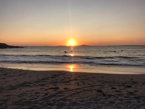 a sunset on the beach with people in the water at Ferry View Cottage in Belmullet