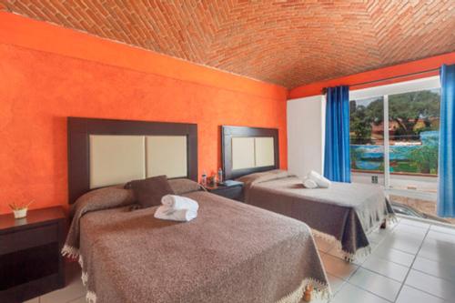 1 dormitorio con 2 camas y pared de color naranja en Posada San Javier, en Tequisquiapan