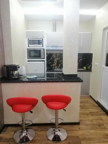 Comforts apartments 1 في فنيدك: مطبخ مع اثنين من المقاعد الحمراء أمام منضدة