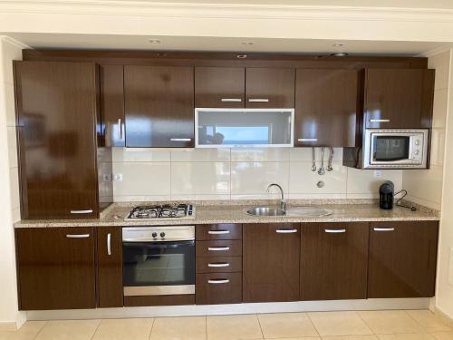 a kitchen with wooden cabinets and a sink and a microwave at LUNA - Airco - Sea view - First line - Own parking in Armação de Pêra