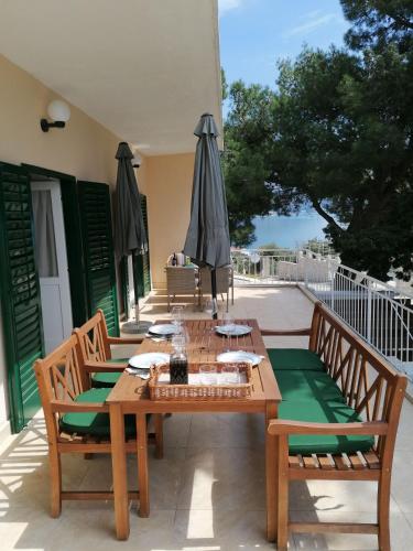 une table et des chaises en bois sur une terrasse avec des parasols dans l'établissement Apartment Borovi with terrace and parking Podaca, à Podaca