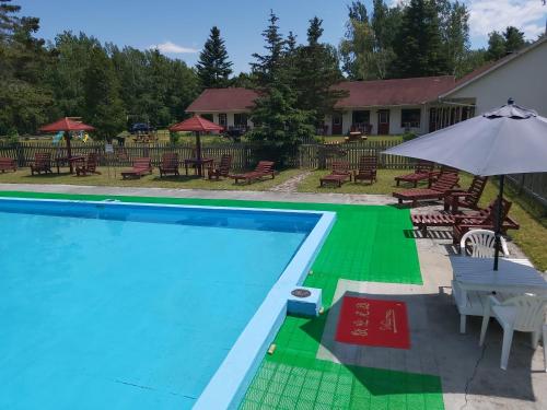 a pool with tables and chairs and an umbrella at Auberge La Coudriere (Cool Hotel) in L'Isle-aux-Coudres