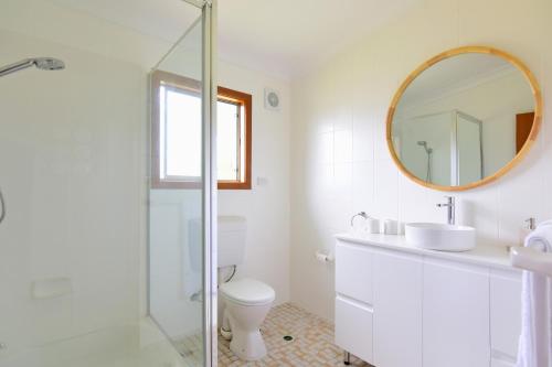 La salle de bains blanche est pourvue de toilettes et d'un miroir. dans l'établissement LAKE146C - Casa Iolanda, à Culburra Beach