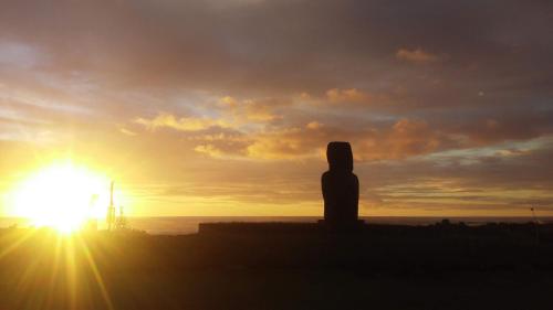 a person sitting on a wall watching the sunset at Cabañas Te Maori in Hanga Roa