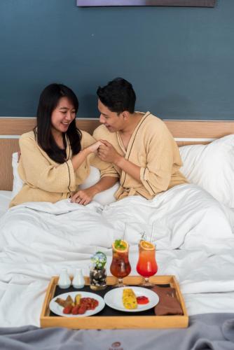 a man and woman sitting in bed with a tray of food at Nava Hotel Tawangmangu in Tawangmangu