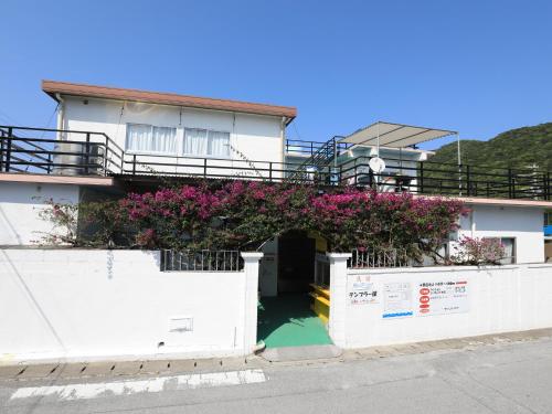 a white building with pink flowers on it at Pension Sea Friend in Tokashiki