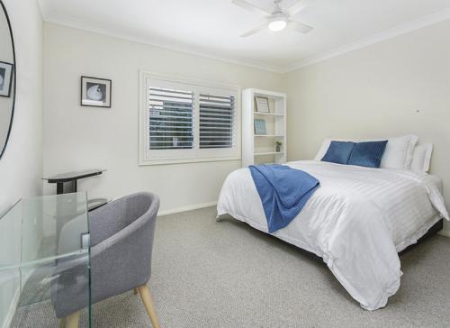 a white bedroom with a bed and a glass table at Shellharbour Seaside Escape in Shellharbour