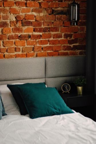 a brick wall behind a bed with a green pillow at BOOGIE Home Kamienica Łódzka in Łódź