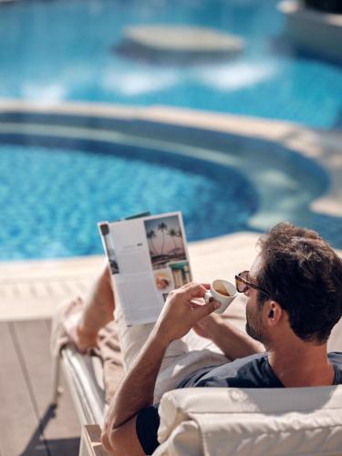 a man laying in a chair reading a book and drinking a coffee at Lesante Classic - Preferred Hotels & Resorts in Tsilivi
