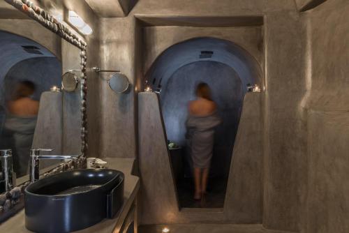 
a man standing in a bathroom next to a sink at Andronis Luxury Suites in Oia
