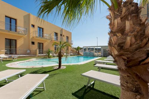 a pool with benches and a palm tree next to a building at Residence Le Piscine in San Vito lo Capo