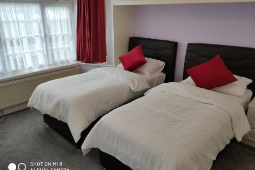 two beds with red pillows in a bedroom at Cozy Entire Bungalow House in Winchmore Hill
