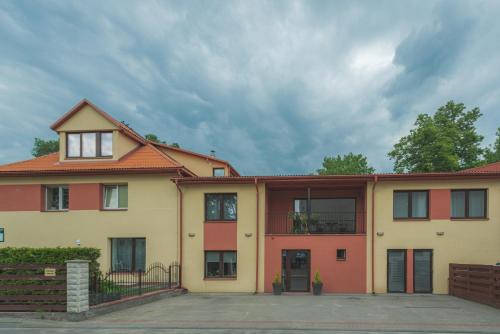 a yellow and orange building with a cloudy sky at Senasis Nemunas in Druskininkai