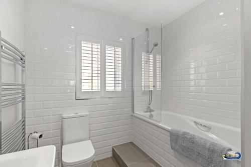 a white bathroom with a toilet and a bath tub at Park Gardens - Lovely Cottage, Parking, Central Location in Begelly