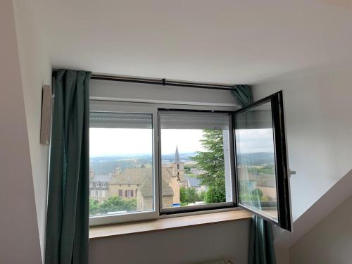 - une fenêtre avec des rideaux verts et une vue sur un bâtiment dans l'établissement La ferme de l'Aubrac, à Aumont-Aubrac