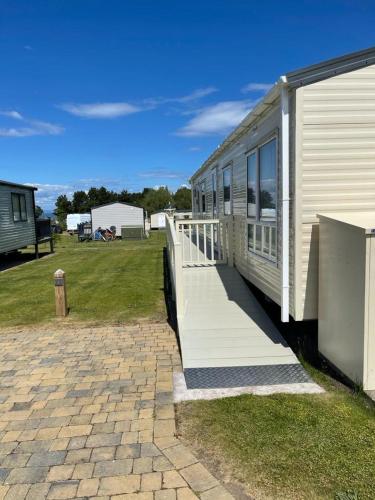 a white building with a porch next to a field at Seton sands holiday park - Premium caravan - 2 bedroom sleeps 4 in Port Seton