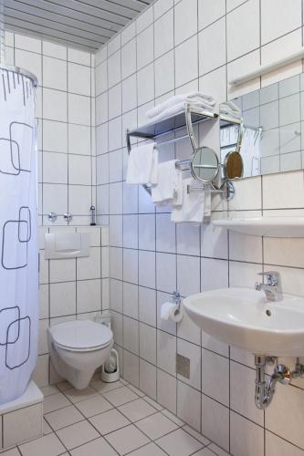 a white tiled bathroom with a toilet and a sink at Hotel Ruppert in Walluf