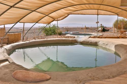 a large pool of water with an umbrella at Desert Days mud cabin's Resort in Zuqim