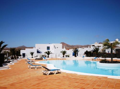 a swimming pool with lounge chairs and buildings at Alojamiento Vacacional con balcón La Vela in Puerto Calero