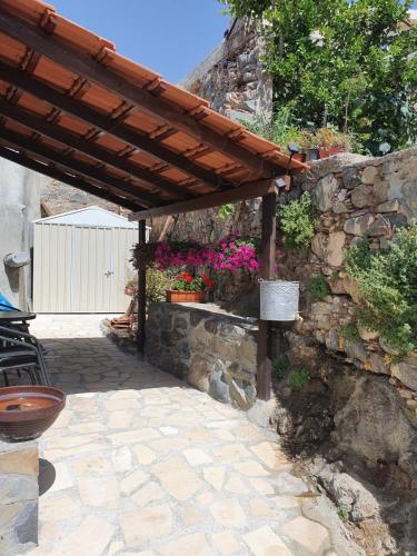 a patio with a stone wall and a wooden pergola at Petradaki House in Arakapas