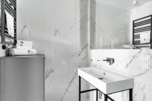 a white bathroom with a sink and marble walls at EL Apartments - Atlas in Poznań