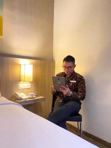 a man sitting in a chair with a laptop in a hotel room at News Hotel Waru Sidoarjo in Waru