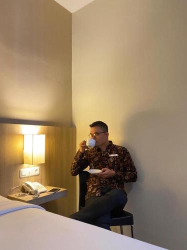 a man drinking a cup of coffee in a hotel room at News Hotel Waru Sidoarjo in Waru