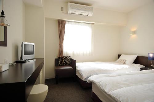 高知市にあるセブンデイズホテルプラスのベッド2台、デスク、テレビが備わるホテルルームです。