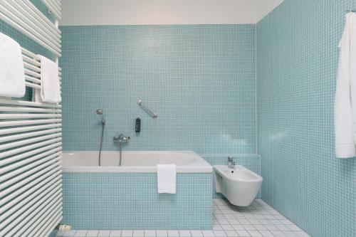 a blue tiled bathroom with a tub and a toilet at Seminaris Hotel Potsdam Griebnitzsee in Potsdam