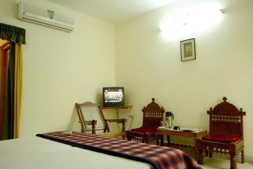 a bedroom with a bed and two chairs and a television at Rising Sun Retreat in Mount Ābu