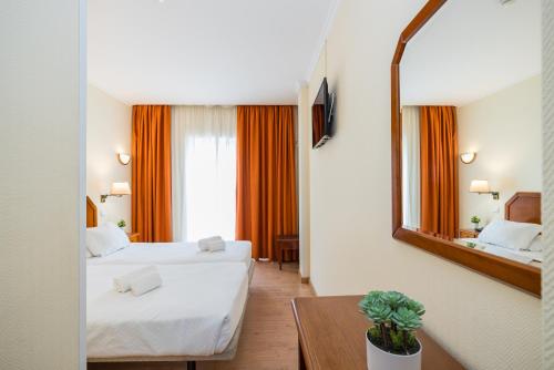 a hotel room with two beds and a mirror at Hotel Residencial Colibri in Costa da Caparica