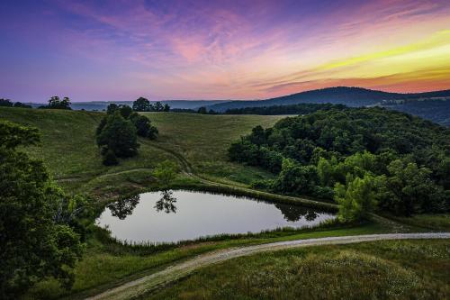 a pond in the middle of a field with a sunset at This is the ultimate in private escape in Ponca