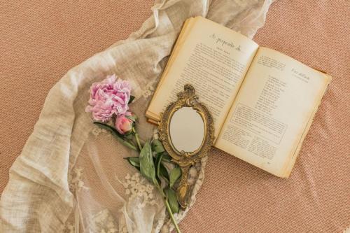 a book with a mirror next to a pink flower at B&B Antico Telaio in Santa Maria Navarrese