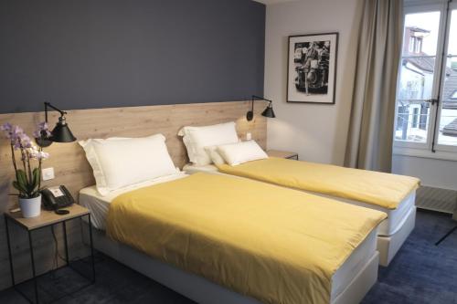 two beds in a hotel room with yellow sheets at Boutique Hôtel de l'Ecu Vaudois in Begnins
