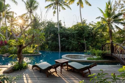 a patio with chairs and a pool with palm trees at Arkamara Dijiwa Ubud in Ubud