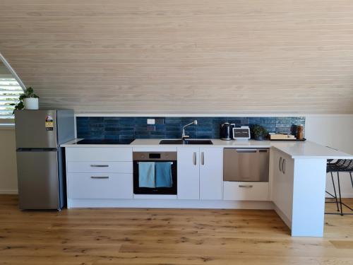 a kitchen with white cabinets and a sink and a refrigerator at The Boatshed, Luxury Waterfront Accommodation in Raglan