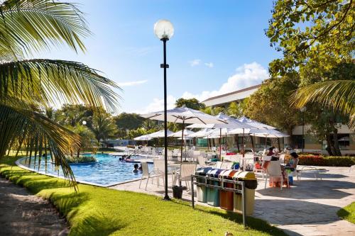 a pool with tables and chairs and people sitting around it at Paraíso na terra - Carneiros Beach Resort in Tamandaré