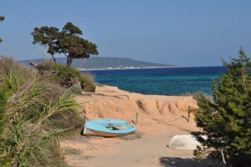 un barco azul sentado en la arena cerca del océano en Paraiso de los Pinos ET241 PL, en Sant Francesc Xavier